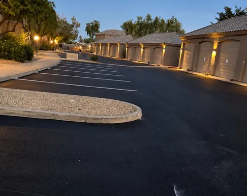 Newly paved asphalt and freshly striped parking spaces along a lit garage row at Talavera HOA after full street reconstruction